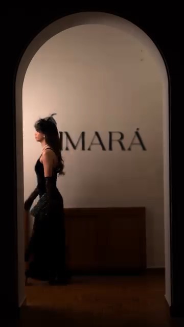 Woman in an elegant black outfit surrounded by candles in a cinematic luxury perfume video production scene.