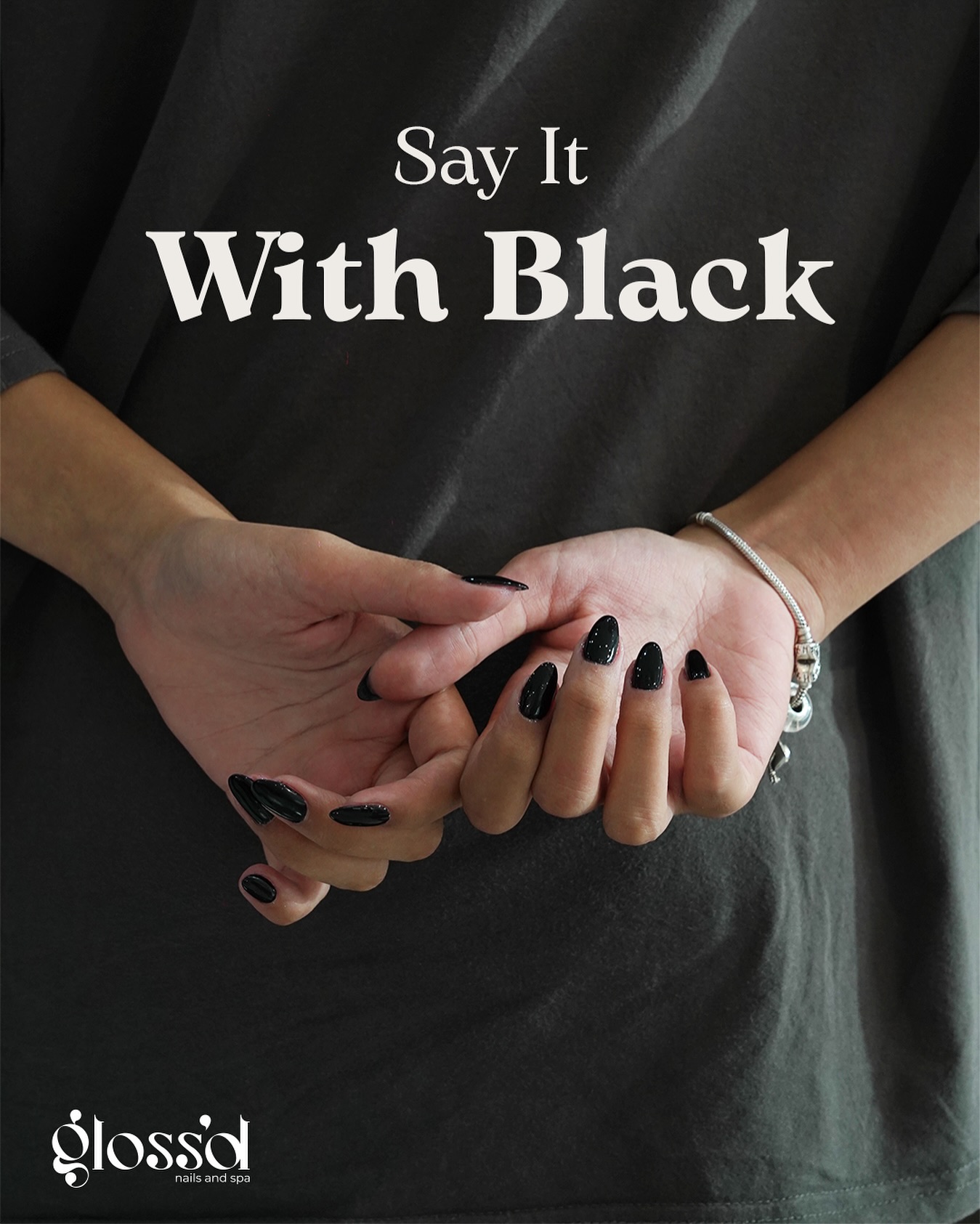 Hands displaying a glossy black manicure with “Say It With Black” text for Glossd nail salon content